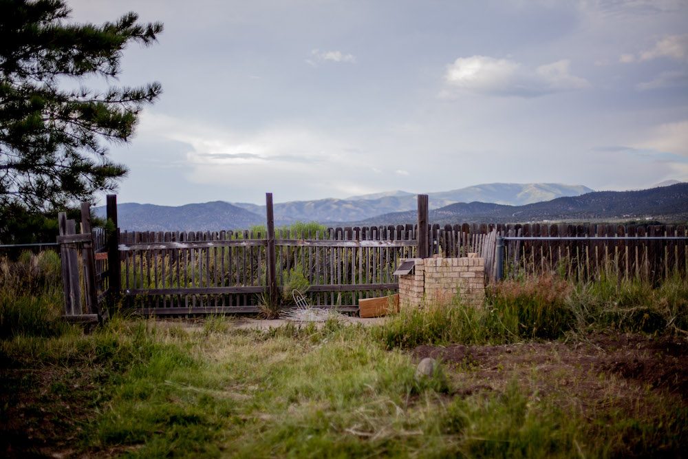 Weathered wooden fence and brick post in front of a mountain range under a cloudy sky