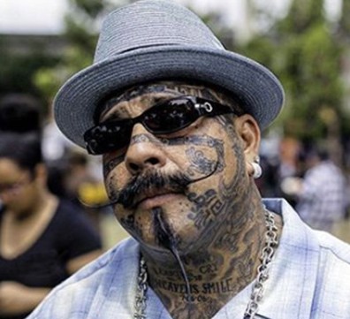 Portrait of a man in a gray fedora and sunglasses with face tattoos